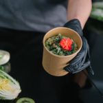 A hand holding a salad bowl with fresh vegetables and a colorful garnish, emphasizing healthy eating.